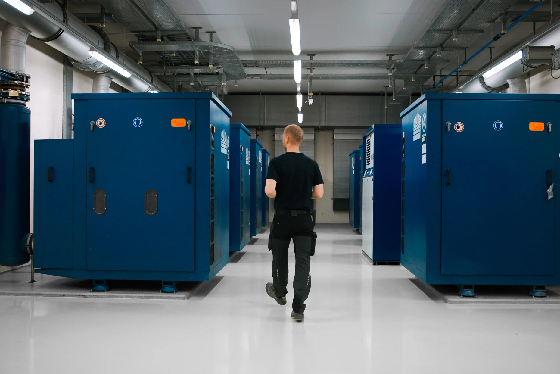 Mitarbeiter geht durch einen Technikraum der ARA Bendern zwischen grossen blauen Anlagen.